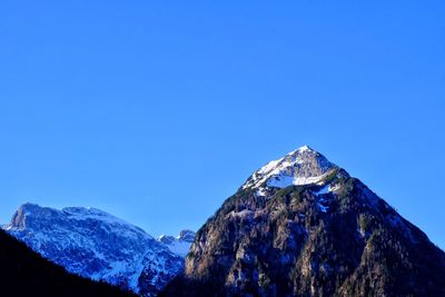 Low angle view of snow covered mountains against blue sky