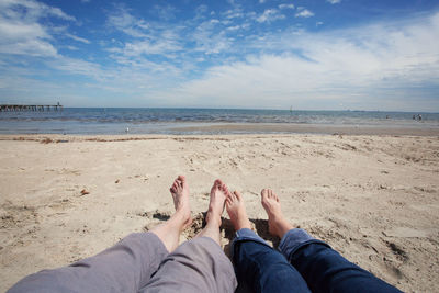 Low section of friends on beach against blue sky