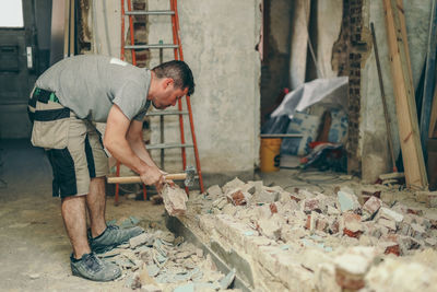 A young man breaks a brick wall with a sledgehammer.
