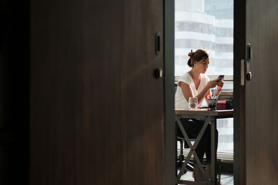 Side view of young woman looking through window