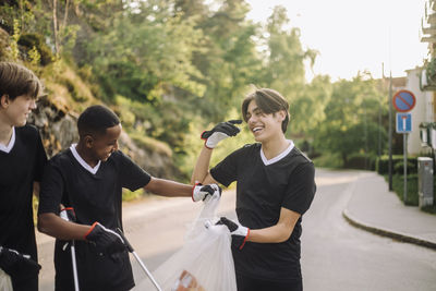 Cheerful teenage boys with garbage bags on road