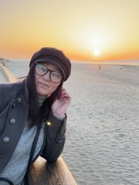 Portrait of young woman at beach against sky during sunset