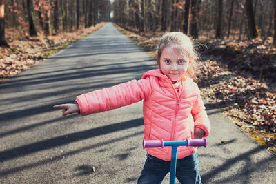 Portrait of cute girl pointing while standing with push scooter