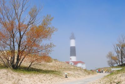Lighthouse amidst trees and buildings against sky with light fog
