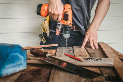 Midsection of carpenter while using drill machine on wooden table