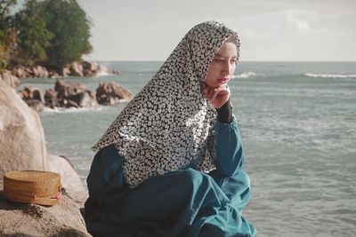 Woman sitting on beach by sea against sky