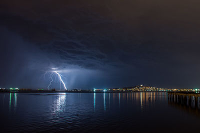 Illuminated city by sea against sky at night