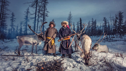 Men standing by reindeer on snow