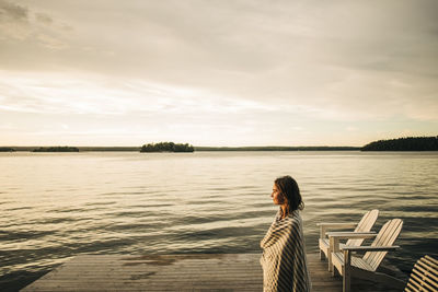 Side view of woman wearing towel while standing on jetty during sunset