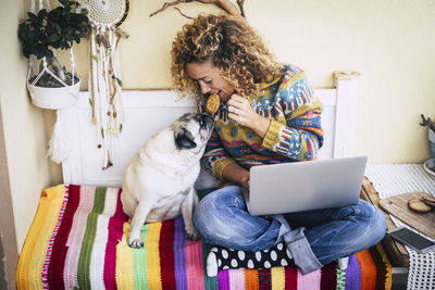 Smiling woman eating food sitting with dog at home