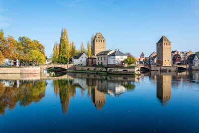 Reflection of buildings and trees in lake against blue sky