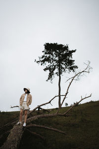 Full length of woman standing on tree trunk against sky