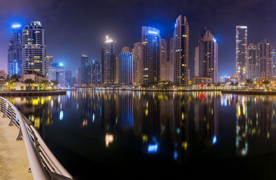 Illuminated buildings by river in city at night