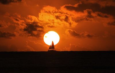Silhouette cross on beach against sky during sunset