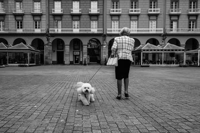 Rear view of woman walking with dog on street against building