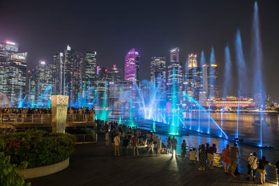 People at spectra show of fountains, colorful light water show along promenade by marina bay sands
