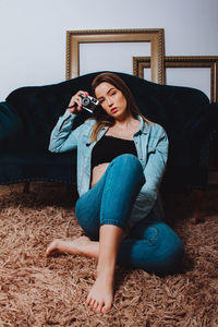 Portrait of woman holding camera sitting by sofa at home