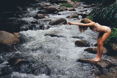 Full length of young woman standing on rock by river