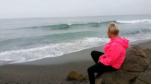 Full length of woman sitting on rock at beach