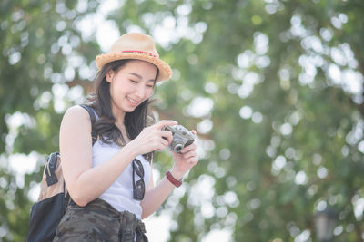 Happy woman photographing against trees