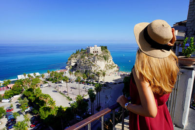 Back view of beautiful young woman enjoying view of tropea village, calabria. summer in italy.