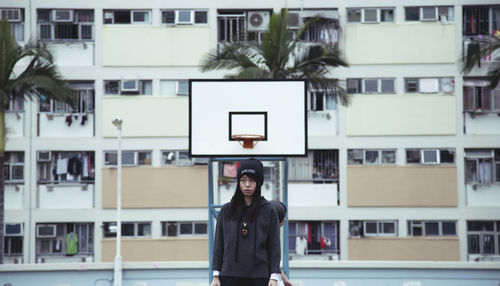 Portrait of young woman standing against building in city