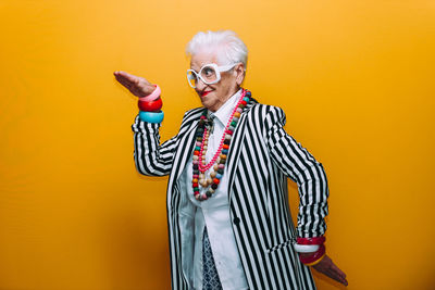 Smiling senior woman gesturing against yellow background