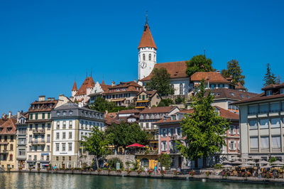 Buildings by river against clear blue sky