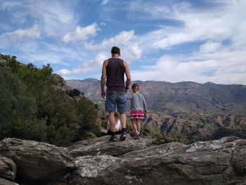 Rear view of man with daughters on cliff against cloudy sky