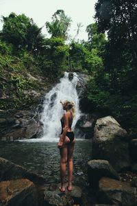 Full length of woman standing on rock against waterfall