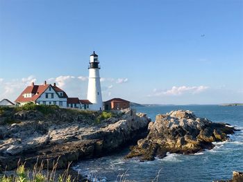 Lighthouse by sea and buildings against sky