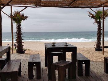 Chairs and table at beach against sky