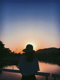 Rear view of woman looking at lake against sky during sunset