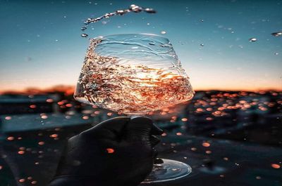 Close-up of water drops on glass against sky during sunset