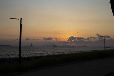 Silhouette street by sea against sky during sunset