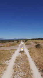 Road passing through field against clear sky