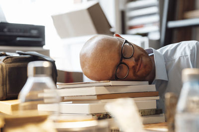 Tired businessman sleeping on books in office