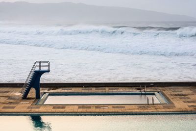 Deck chairs by swimming pool against sky