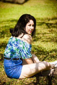 Side view of beautiful young woman looking away while sitting on grassy field at park