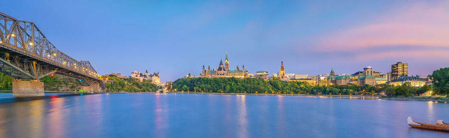 Panoramic view of buildings by river against sky in city