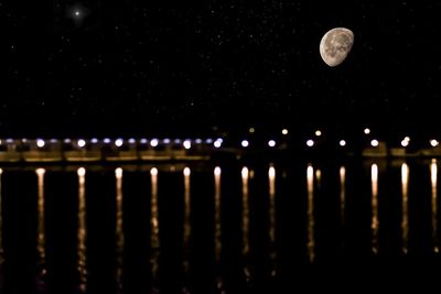 Reflection of illuminated lights in river against sky at night