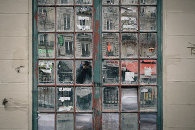 Reflection of person photographing seen on glass door