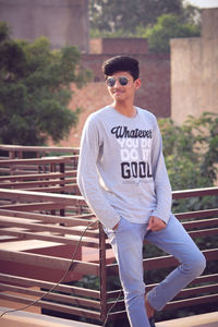 Young man wearing sunglasses standing by railing outdoors