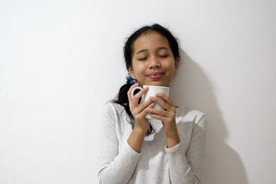 Young woman holding camera against wall