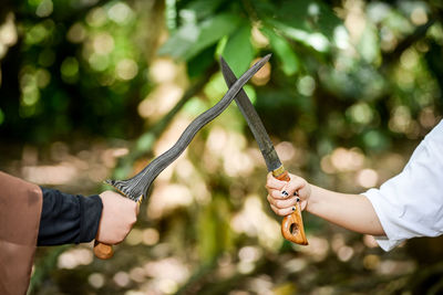 Cropped image of warriors holding swords fighting at forest