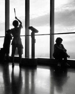 Silhouette people standing by window against sky