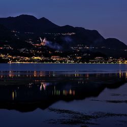 Illuminated city by lake against sky at night