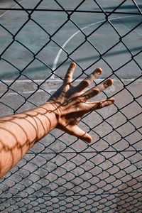 Hand with shadow shapes grabbing a metallic fence