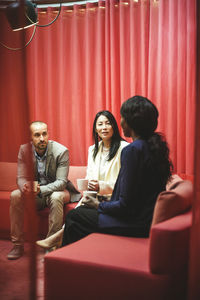 Male and female coworkers drinking coffee while discussing on sofa in office