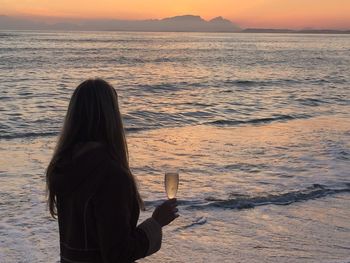 Side view of woman holding champagne flute at beach during sunset